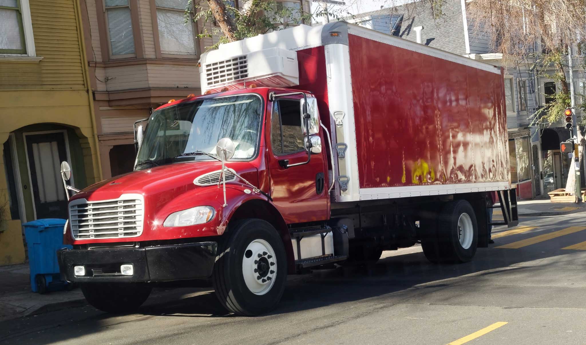 Front and side view of shiny red refrigerated delivery truck park in urban neighborhood.